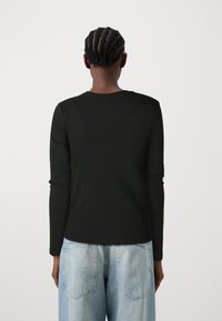 Zwarte top met lange mouwen van gladde stof, met een ronde hals en fitted mouwen, gecombineerd met lichtblauwe, losse jeans.