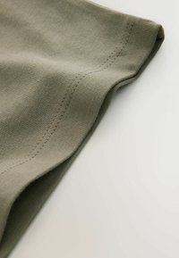 Tkanina oliwkowozielona o gładkiej fakturze i widocznym przeszyciu; krawędź jest podwinięta, ukazując czyste wykończenie i delikatne prążkowanie.