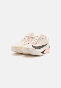 Fodtøj med en beige mesh-overdel, sort swoosh, ferskenfarvede accenter og en struktureret hvid sål med lyserøde detaljer.