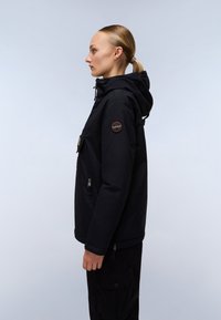Black hooded jacket with zippered pockets, a textured fabric, and a circular logo patch on the sleeve. Model shown in profile.