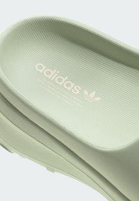 Sapatilha slip-on verde texturizada com forma contornada. Apresenta marcação em relevo e um design de biqueira suave e arredondada.