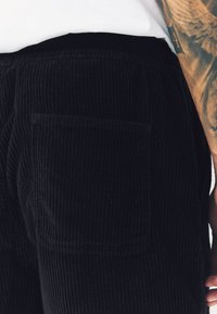 Zwarte corduroybroek met een gestructureerde stof met verticale strepen, een opgestikte achterzak en een elastische tailleband.