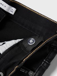 Jeans en denim noir avec une fermeture éclair et un bouton à l'avant. Coutures notables en marron clair et étiquette en tissu indiquant "JEANS PAR NAME IT."