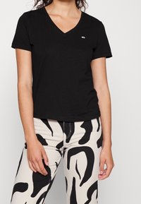 Czarny t-shirt z dekoltem w serek, wykonany z miękkiej bawełny, z krótkimi rękawami i małym logo, połączony z kremowymi spodniami z wyraźnym czarnym wzorem.