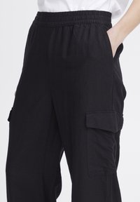 Pantalons cargo noirs avec une taille élastique, des poches latérales et une texture lisse. Présente une coupe décontractée et plusieurs poches de style cargo.