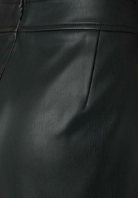 Jupe en cuir noir avec une texture lisse, dotée d'une poche avant. La surface présente un léger éclat et des détails cousus le long de la taille.