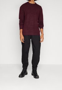 Bordo neulepaita, jossa on teksturoitu kuvio, pyöreä kaula-aukko ja ribbineulokset hihansuissa, yhdistetty mustiin housuihin ja mustiin nauhakenkiin.