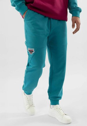 Türkisfarbene Jogginghosen aus weichem Stoff mit schmaler Passform, versehen mit einem dreieckigen Patch am linken Oberschenkel und seitlichen Taschen.