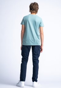 Světle modré bavlněné tričko s kulatým výstřihem, v kombinaci s tmavě modrými cargo kalhotami se bočními kapsami a elastickými manžetami, nošeno s bílými teniskami.