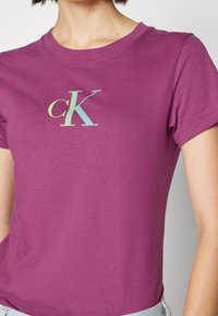 Fialové tričko s krátkým rukávem se multibarevným logem "ck". Vyrobeno z měkké a hladké látky s klasickým kulatým výstřihem.