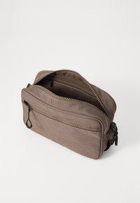 Ruskea kangaskassi vetoketjulla varustettuna, jossa on etutasku ja karhea pinta. Sisältää pienen lenkin kiinnitystä varten.