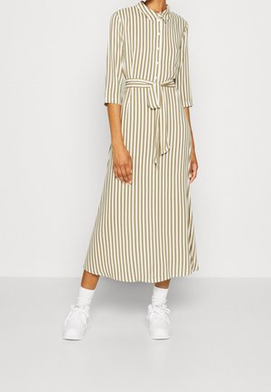 Gestreepte midi jurk in roomwit en olijfgroen met een kraag met knopen, driekwart mouwen en een tailleband. Draagt met witte sneakers.