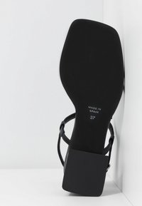 Sandale noire à talon avec un bout carré, une semelle texturée et des fines lanières. Taille 37, marquée "Fabriqué en Espagne" sur la semelle.