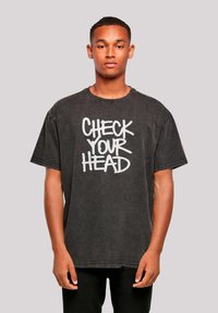 Black cotton t-shirt featuring a graphic print with the text "CHECK YOUR HEAD" in white, short sleeves, and a relaxed fit.
