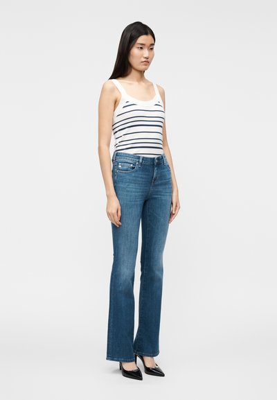 Τζιν παντελόνι με καμπάνα σε μέτρια βαφή, συνδυασμένο με λευκό τοπ με ναυτικές ρίγες. Το μοντέλο φοράει μαύρες �γόβες με μυτερή μύτη.