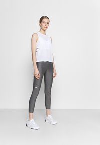 Vit ärmlös mesh-topp som är parat med åtsittande grå leggings. Leggings har en subtil melerad textur och logotypdetalj på underbenet.