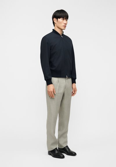 Ναυτικό μπουφάν βομβαρδισμού με φερμουάρ μπροστά, μανσέτες με ρίγες, σε συνδυασμό με ανοιχτό γκρι παντελόνι και μαύρα επίσημα παπούτσια. Μινιμαλιστικός σχεδιασμός και εφαρμογή.