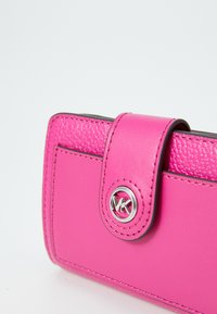 Fuchsia læderpung med tekstureret finish, der har et sølvlogo og en snaplukning. Inkluderer kontrasterende syninger.