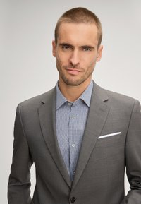 Gray tailored suit jacket over a light blue patterned shirt, featuring a white pocket square and a buttoned collar. Smooth, structured fabric.