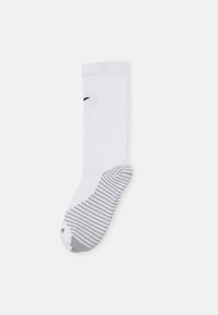 Chaussette de sport blanche avec texture côtelée, un logo noir et un talon gris avec un design rayé en bas.