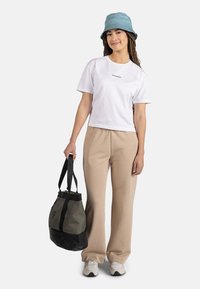 Camiseta corta blanca con el texto "ROSSIGNOL", pantalones beige de pierna ancha, sombrero de cubo gris y una bolsa negra/gris con correas ajustables.