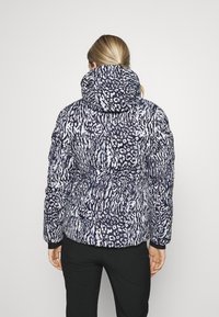 Veste matelassée à col montant, présentant un motif animalier noir et blanc, des poignets élastiques et une silhouette ajustée.