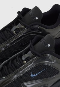 Juodos sportinės kedės su tinklelio ir sintetiniu viršumi, akcentuotu ryškiu Nike swoosh, su tekstūriniais akcentais ir juodomis raištelėmis.