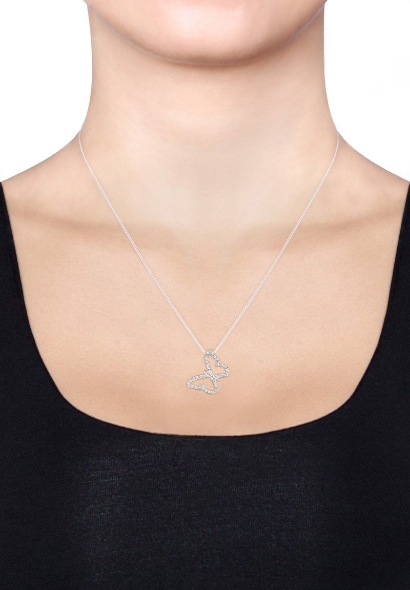 Collier en argent en forme de papillon avec une chaîne délicate, mettant en valeur des accents en cristal scintillants. Le design du papillon est ouvert et détaillé, reposant au-dessus d'un haut noir.