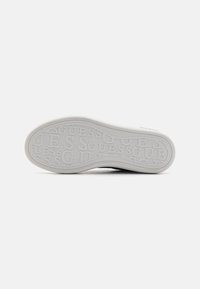 Schuhsohle aus weißem Gummi mit geprägt "GUESS" Muster. Gekrümmte Form mit einer strukturierten Griffoberfläche. Keine sichtbaren Akzente oder Markierungen.