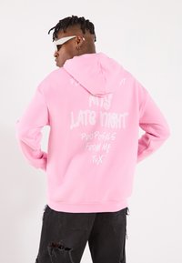 Felpa con cappuccio rosa con testo bianco sulla schiena, che presenta frasi come "Late Night" e "Proposals From Me THX". Indossata con jeans neri strappati.