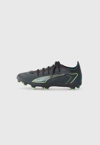 Black soccer cleat with textured upper, green highlights, and a streamlined design. Features a lace-up closure and molded studs for traction.