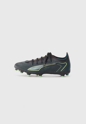 Black soccer cleat with textured upper, green highlights, and a streamlined design. Features a lace-up closure and molded studs for traction.