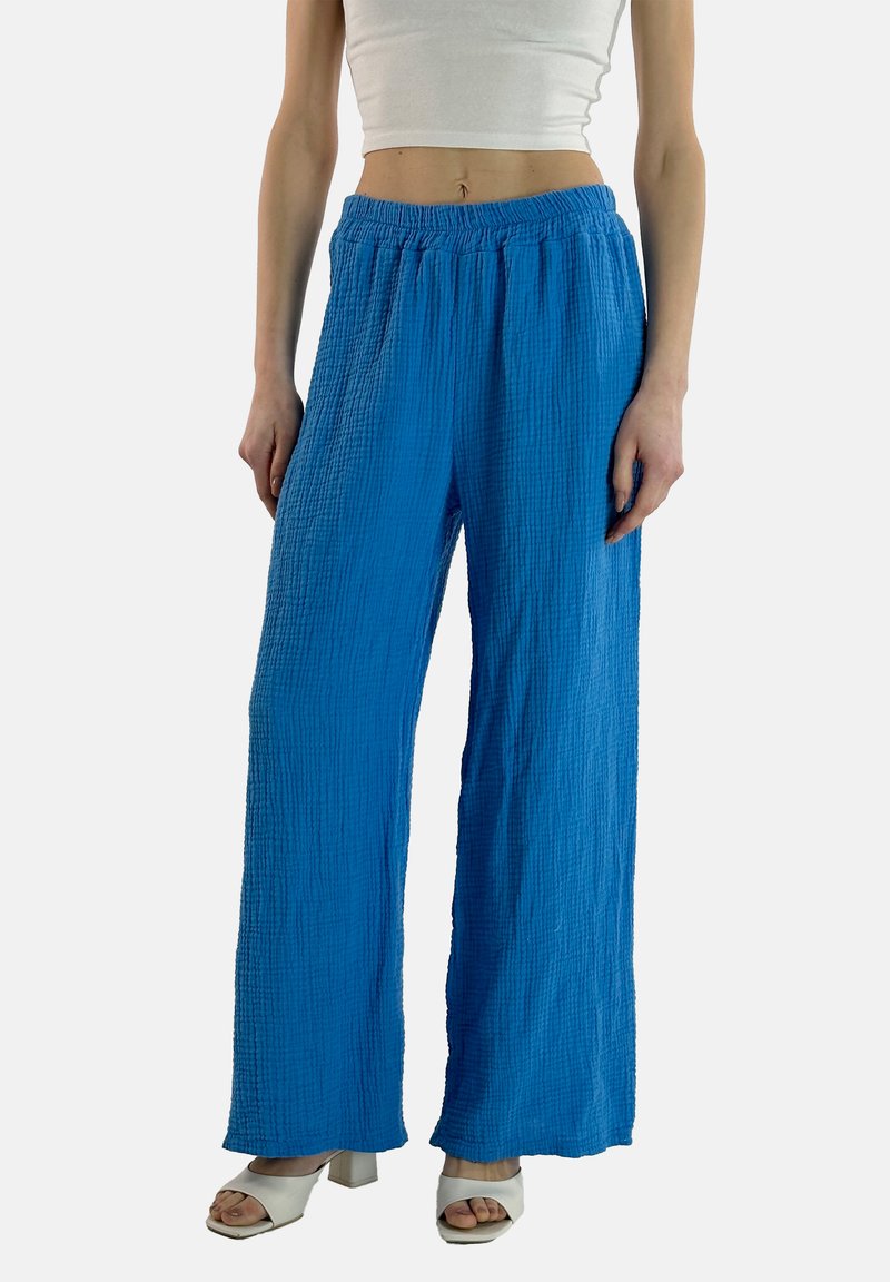 Pantaloni larghi blu, testurizzati, con vita elasticizzata, caratterizzati da un design di tessuto stropicciato e tasche laterali. Abbinati a tacchi bianchi.