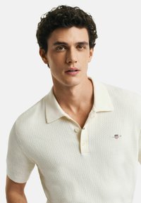 Eisi kremfarbener Poloshirt mit kurzen Ärmeln, strukturiertem Muster, einer Drei-Knopf-Leiste und kleinem gesticktem Logo auf der linken Brust.