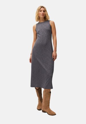 Mujer con un vestido midi de canalé gris sin mangas y botas vaqueras de ante marrón claro, de pie frente a un fondo blanco liso.