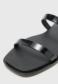 Černé sandály s dv�ěma lesklými popruhy, texturovanou stélkou a čtveratou špičkou. Podešev je hladká a mírně zvýšená.