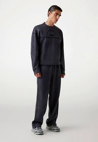 Dark gray sweatshirt and matching joggers made of soft fabric. Sweatshirt features a round neckline and logo detail; pants have an elastic waistband.