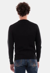 Maglione nero a maniche lunghe con collo tondo, realizzato in tessuto liscio, con design aderente e orlo dritto, abbinato a jeans di denim blu.