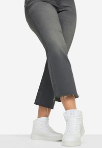 Jeans large gris avec ourlet effiloché, associés à des baskets montantes blanches. Les jeans présentent une texture subtile et un design en denim classique.