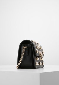 Borsa a tracolla in pelle nera con accessori in oro, con accenti a borchie e una tracolla in catena. Forma compatta con chiusura a soffietto e superfici testurizzate.