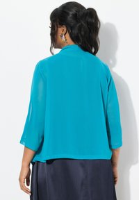 Turkoosi läpikuultava kimono-takki, jossa on 3/4 hihet, väljä malli ja hieman pidempi takapuoli. Yhdistetty tummansiniseen, valuvaan hameeseen.