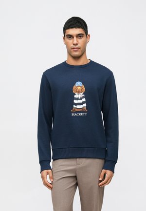 Marineblå sweatshirt med et bjørn grafik iført en stribede skjorte og kasket; ribbede manchetter og kant; logoet "HACKETT" under grafikken.