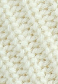Primo piano di un morbido e spesso filato bianco lavorato a maglia con un motivo testurizzato, dove anelli intrecciati creano una superficie tessile accogliente.