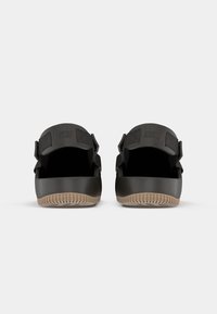 Crne klizne sandale s gumeni đon, podesivim remenom s čičak zatvaranjem i "NIKE" utisnutim na remenu. Bež potplat s teksturom za bolje prianjanje.