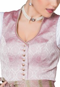 Rosa gemusterte Stoffweste mit V-Ausschnitt, ausgestattet mit sechs Knöpfen, die mit einem Blumenmuster verziert sind, und kombiniert mit einer weißen Bluse darunter.