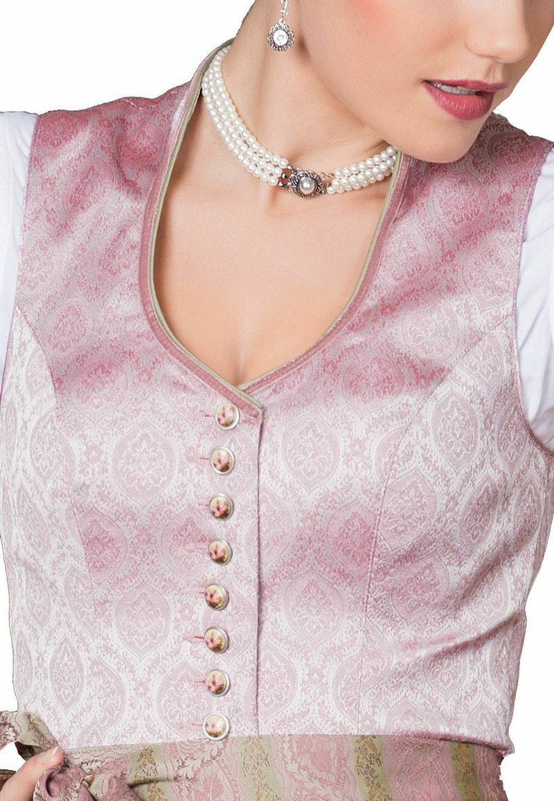 Rosa gemusterte Stoffweste mit V-Ausschnitt, ausgestattet mit sechs Knöpfen, die mit einem Blumenmuster verziert sind, und kombiniert mit einer weißen Bluse darunter.