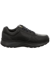 Zapatilla deportiva negra con cuero perforado, punta redonda, suela plana de goma y diseño de cordones. Presenta un branding sutil y acentos texturizados.