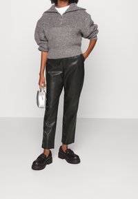 Gray knitted pullover with a half-zip collar, black faux leather trousers, and black platform loafers. Silver handbag with a curved handle.