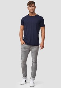 Camiseta de manga corta de color marino combinada con jeans ajustados gris claro y zapatillas blancas con acentos negros. Conjunto simple y casual.
