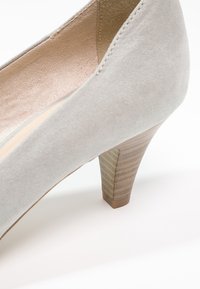 Chaussure à talon haut en daim gris avec un talon effilé. L'intérieur est doublé de doux tissus, et le talon présente une texture à rayures verticales.